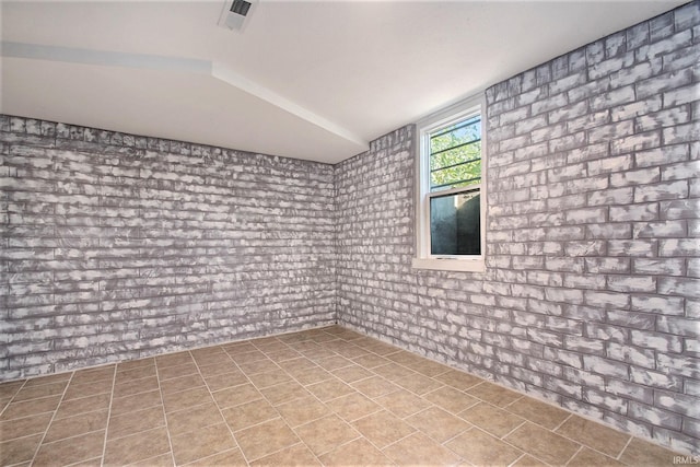 spare room featuring brick wall, vaulted ceiling, and tile patterned floors