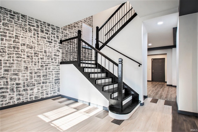 staircase featuring wood-type flooring and brick wall