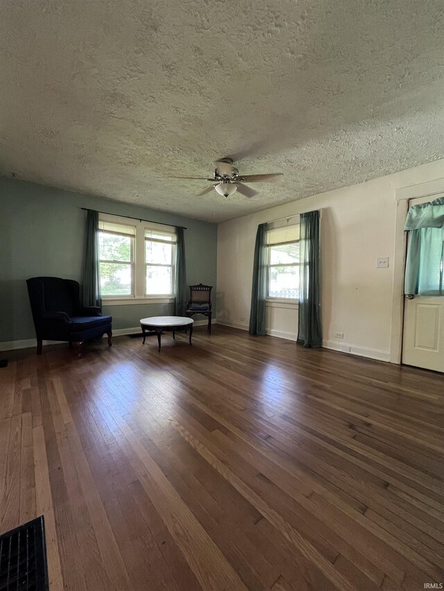 unfurnished living room featuring ceiling fan, dark wood-type flooring, and a textured ceiling