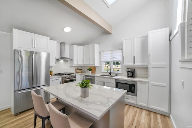 kitchen with appliances with stainless steel finishes, light hardwood / wood-style flooring, wall chimney exhaust hood, sink, and vaulted ceiling with beams