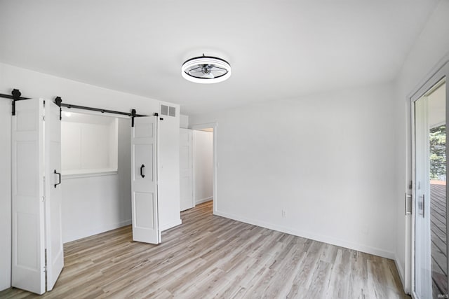 unfurnished bedroom with light wood-type flooring and a barn door