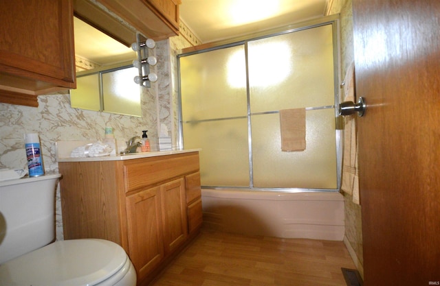 full bathroom featuring shower / bath combination with glass door, vanity, wood-type flooring, tile walls, and toilet