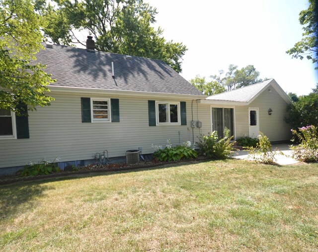 rear view of house featuring central AC and a lawn