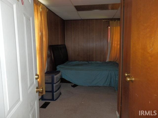 carpeted bedroom with wooden walls and a paneled ceiling