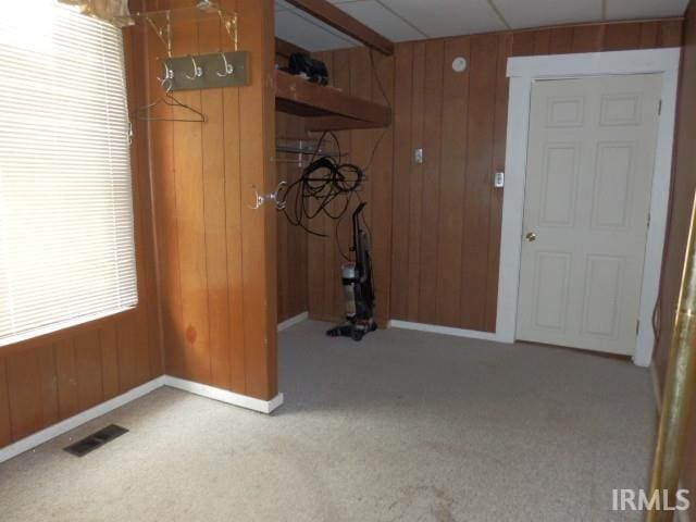 interior space featuring wood walls, a drop ceiling, and carpet flooring