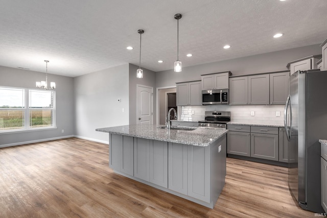 kitchen with appliances with stainless steel finishes, backsplash, a sink, and gray cabinetry