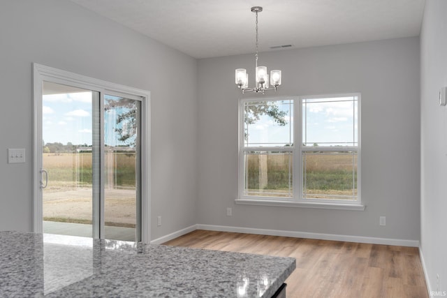 unfurnished dining area featuring baseboards, light wood-type flooring, an inviting chandelier, and a healthy amount of sunlight