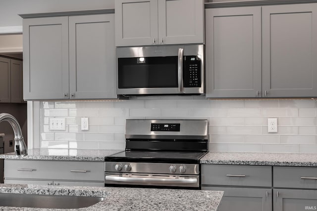 kitchen with appliances with stainless steel finishes, a sink, light stone countertops, gray cabinets, and backsplash