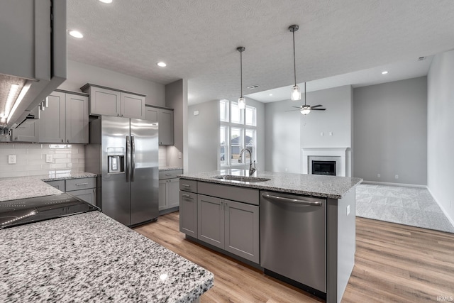 kitchen featuring a glass covered fireplace, appliances with stainless steel finishes, gray cabinetry, light wood-style floors, and a sink