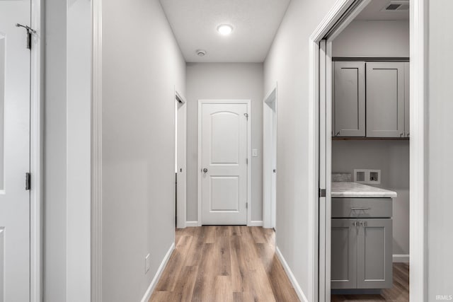 corridor with light wood-type flooring, visible vents, and baseboards