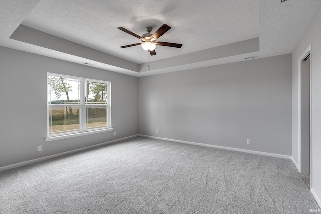 empty room with a textured ceiling, a tray ceiling, carpet flooring, and baseboards