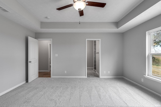 unfurnished bedroom featuring baseboards, multiple windows, and a tray ceiling