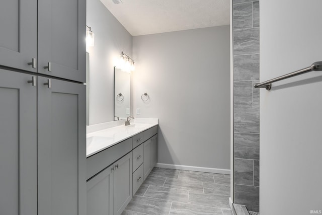 full bath with a sink, a textured ceiling, baseboards, and double vanity