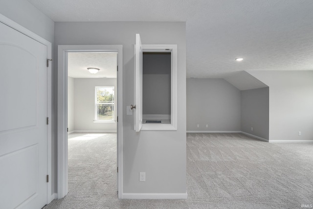 additional living space featuring a textured ceiling, vaulted ceiling, carpet flooring, and baseboards