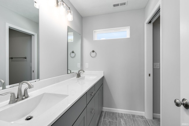 full bath featuring double vanity, a sink, visible vents, and baseboards