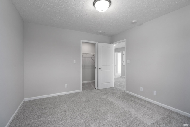 unfurnished bedroom with a textured ceiling, carpet flooring, baseboards, a closet, and a walk in closet