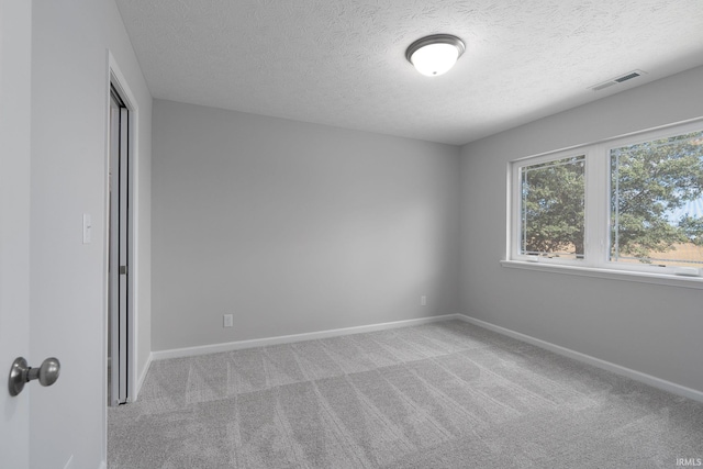 carpeted empty room featuring visible vents, a textured ceiling, and baseboards