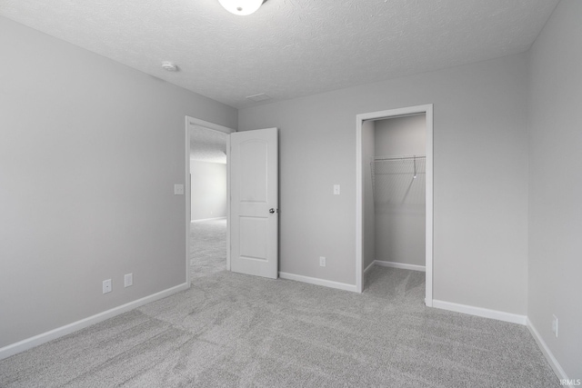 unfurnished bedroom with a textured ceiling, a spacious closet, carpet flooring, and baseboards