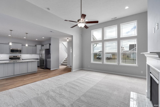 unfurnished living room with light carpet, visible vents, baseboards, stairs, and a fireplace