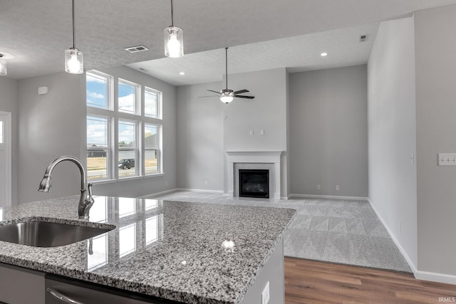 kitchen featuring a fireplace with flush hearth, a sink, visible vents, baseboards, and hanging light fixtures