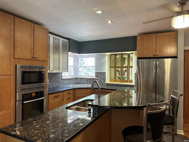 kitchen featuring appliances with stainless steel finishes, a kitchen island with sink, dark stone countertops, and tasteful backsplash