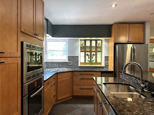 kitchen with sink, dark stone countertops, appliances with stainless steel finishes, dark tile patterned flooring, and decorative backsplash