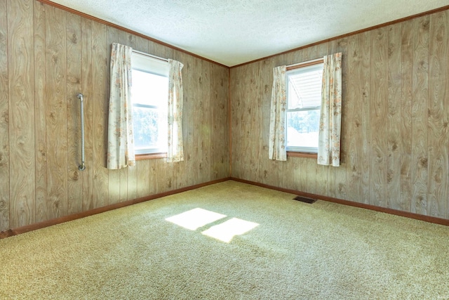 spare room with a textured ceiling, carpet floors, visible vents, baseboards, and crown molding