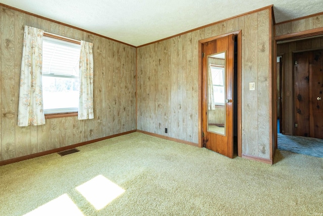 empty room with a textured ceiling, visible vents, baseboards, ornamental molding, and carpet