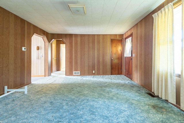 unfurnished room with carpet floors, wood walls, and visible vents