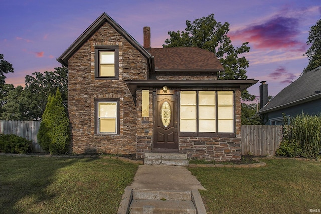 view of front of home featuring stone siding, a front lawn, and fence