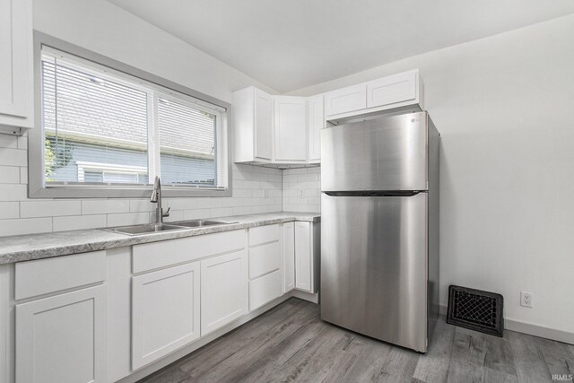 kitchen featuring tasteful backsplash, stainless steel refrigerator, white cabinetry, light hardwood / wood-style floors, and sink