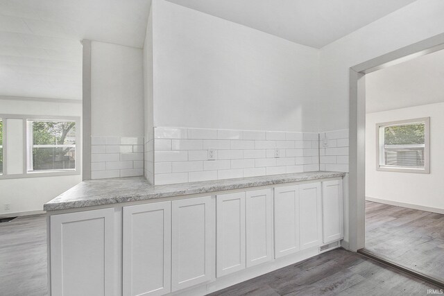 kitchen with decorative backsplash, a healthy amount of sunlight, wood-type flooring, and white cabinetry