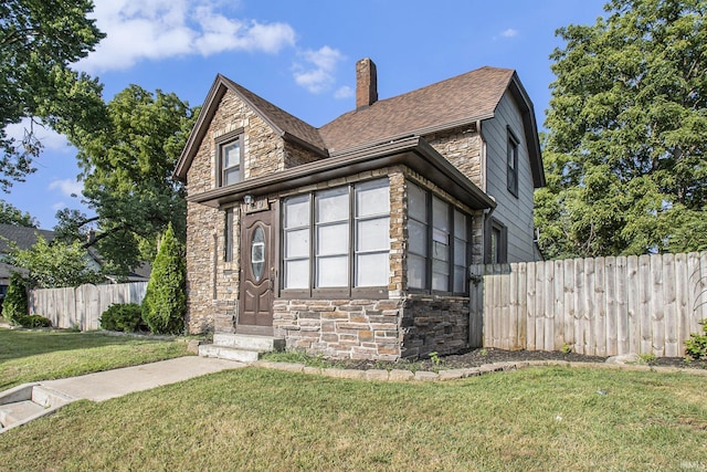 view of front facade featuring stone siding, a chimney, a front yard, and fence