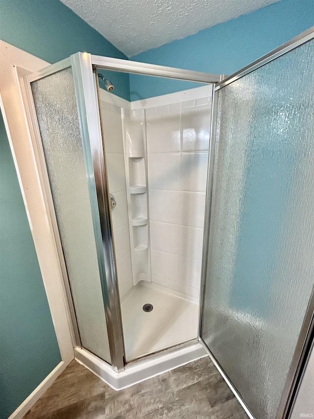 full bathroom with a textured ceiling, a stall shower, and wood finished floors