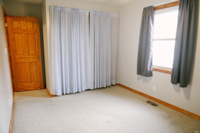 unfurnished room with carpet, visible vents, and baseboards