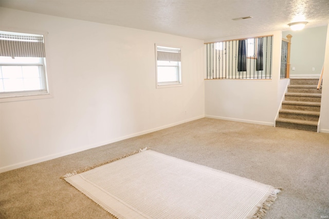 empty room featuring a textured ceiling, carpet floors, stairway, and baseboards