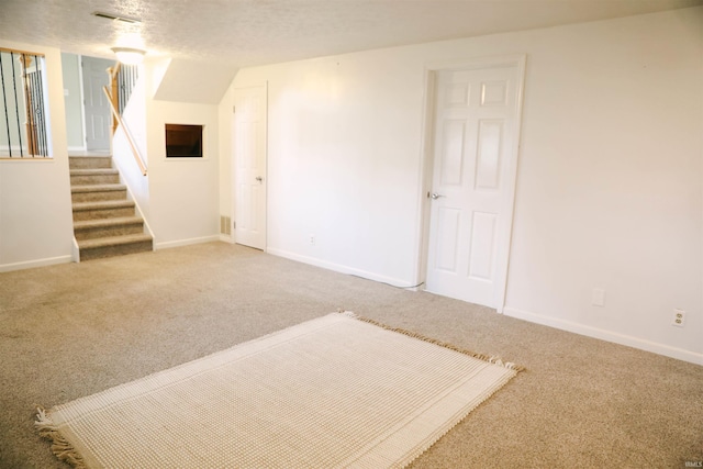 finished basement featuring carpet, visible vents, stairway, and a textured ceiling