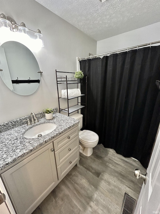 full bathroom with visible vents, toilet, wood finished floors, a textured ceiling, and vanity