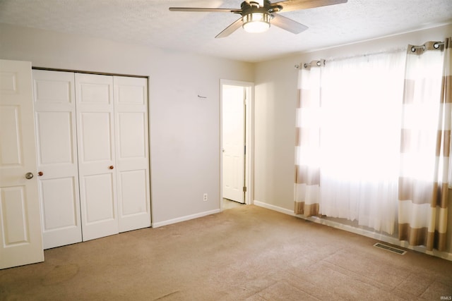 unfurnished bedroom featuring a closet, visible vents, light carpet, a textured ceiling, and baseboards