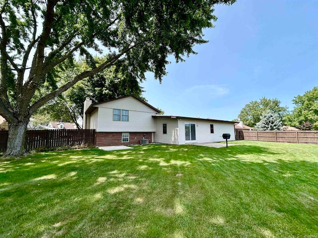 rear view of property with brick siding, a fenced backyard, a lawn, and a patio