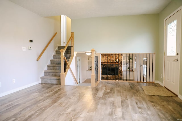 unfurnished living room featuring stairs, a fireplace, baseboards, and wood finished floors