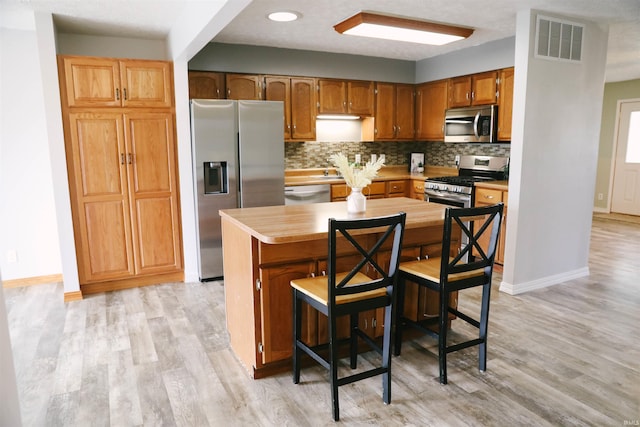 kitchen with light wood-style flooring, visible vents, stainless steel appliances, and backsplash