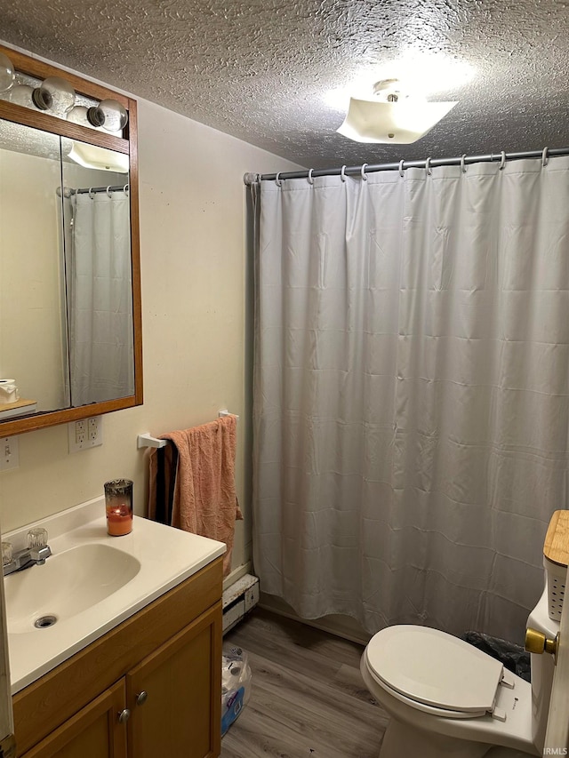 bathroom featuring toilet, vanity, a textured ceiling, wood-type flooring, and a baseboard heating unit