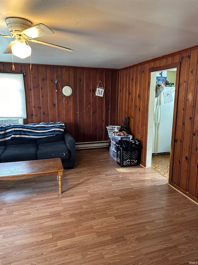 living room featuring a baseboard radiator, ceiling fan, wood-type flooring, and wooden walls