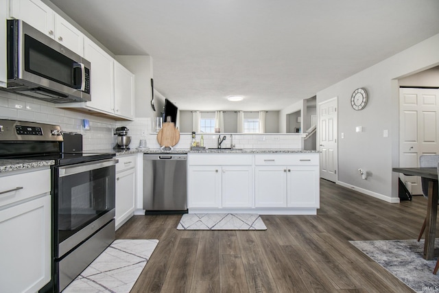 kitchen featuring stainless steel appliances, a peninsula, a sink, white cabinets, and tasteful backsplash