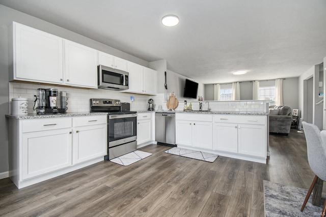 kitchen featuring decorative backsplash, appliances with stainless steel finishes, open floor plan, a peninsula, and white cabinetry