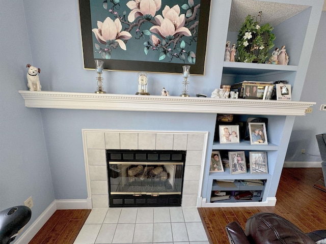 interior details with built in shelves, a tiled fireplace, wood finished floors, and baseboards