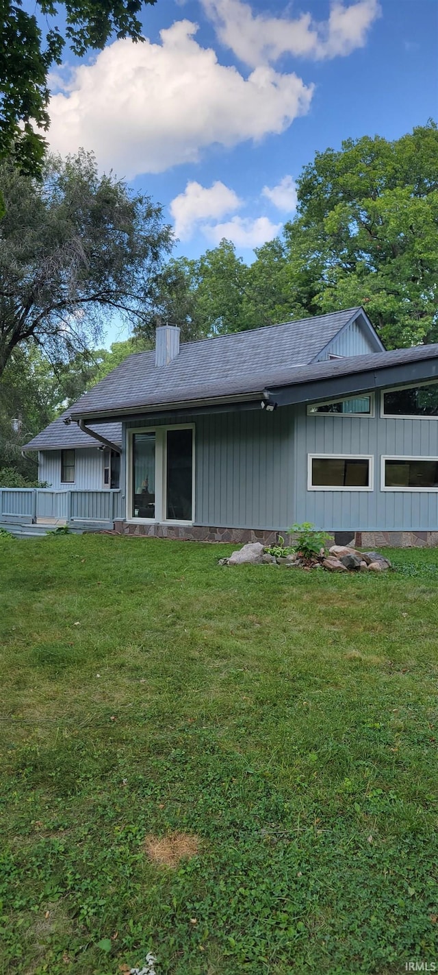 rear view of house with a yard, a shingled roof, board and batten siding, and a chimney