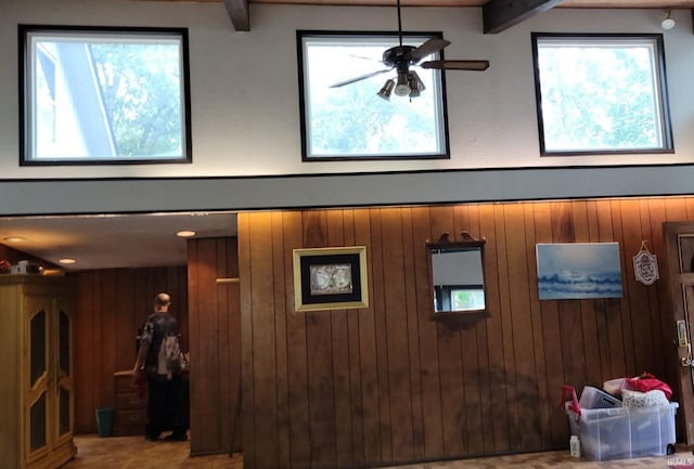 interior space featuring ceiling fan, beamed ceiling, wooden walls, and carpet floors