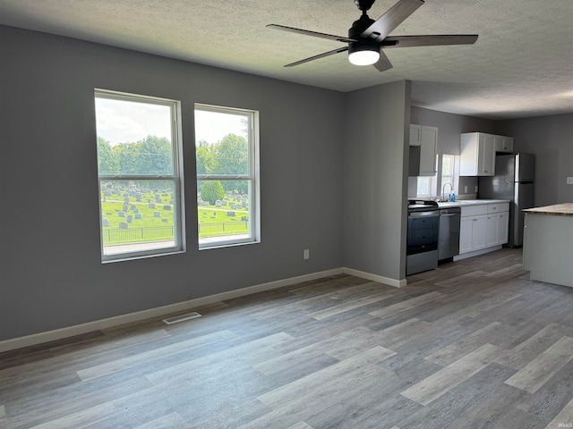 interior space with light hardwood / wood-style floors, dishwasher, ceiling fan, fridge, and white cabinets